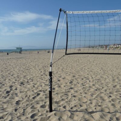 A beach volleyball net on the sand near the ocean.