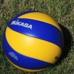 A blue and yellow volleyball sitting on top of grass.