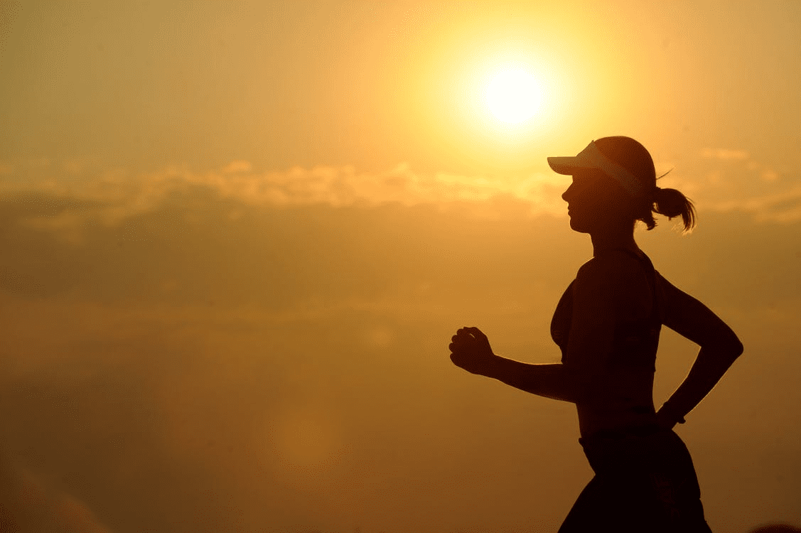 A woman running in the sunset on a hill.