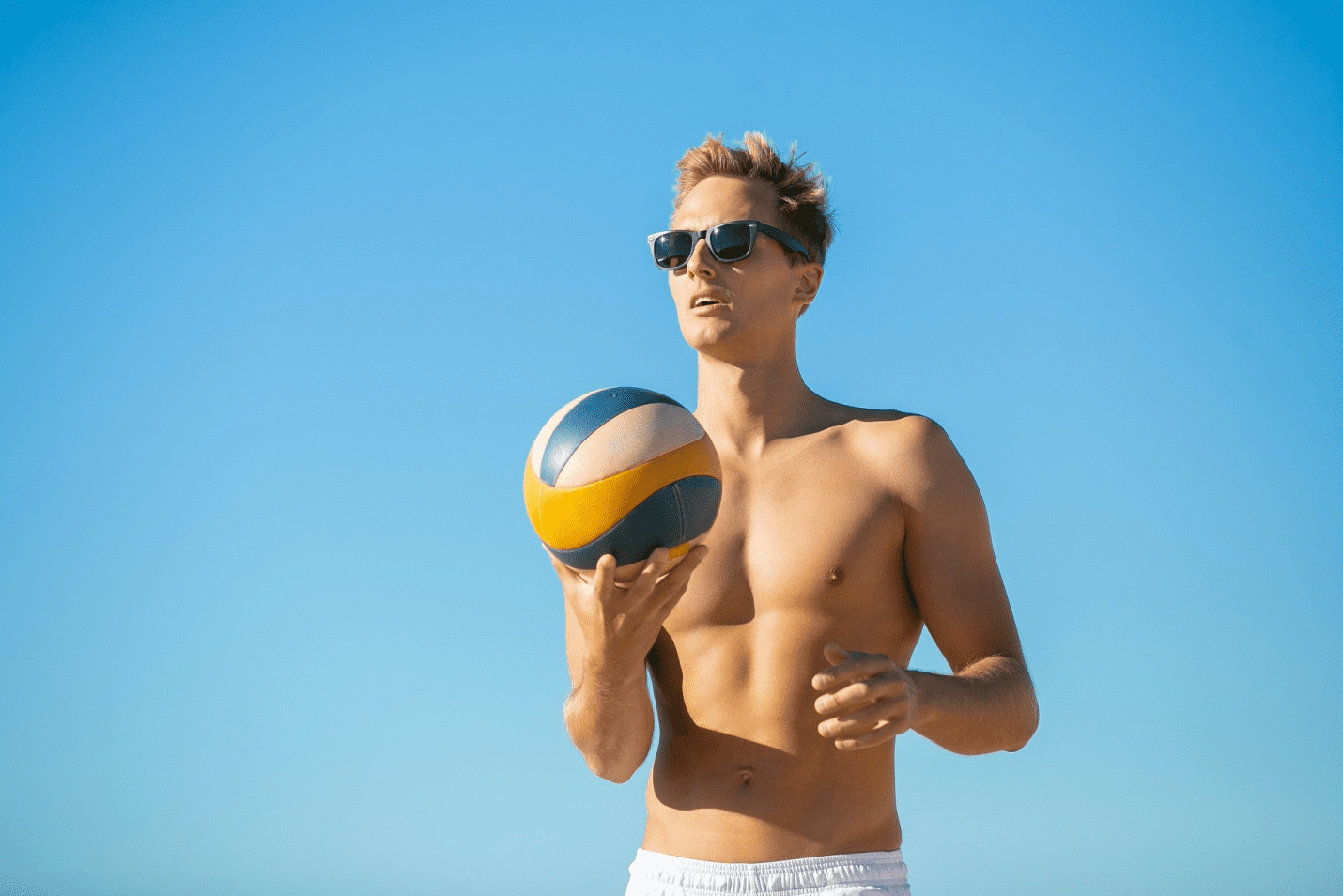 Boy wearing sunglasses holding a volleyball in his right hand