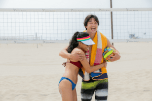 A man holding a volleyball at the beach while hugging a woman as they both smile
